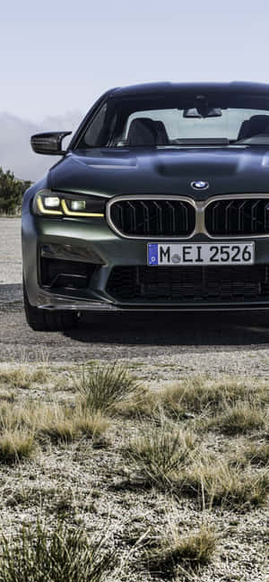 消光黑色BMW M5停放在碎石上，有乾草和遠山。 — Galaxy A07s 壁紙