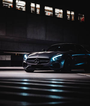 一輛黑色梅賽德斯-AMG GT在夜晚停放在天橋下，車頭燈在濕漉漉的路面上閃爍。 — Galaxy Z Fold 6 壁紙