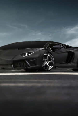 消光黑色藍寶堅尼 Aventador 配碳纖維飾邊，停在黑暗道路上，天空灰色。 — 悟空黑 iPhone 壁紙