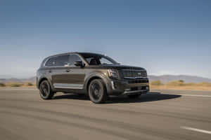 深灰色Kia Telluride SUV在沙漠公路日落時分行駛。 — Surface Laptop 壁紙