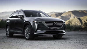 深灰色Mazda CX-9 SUV在日落時停泊在沙漠山丘附近的碎石上。 — 馬自達 壁紙