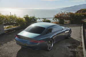 時尚的藍色 Genesis X 汽車停泊在懸崖上，俯瞰夕陽下的海洋。 — MacBook Air M3 壁紙