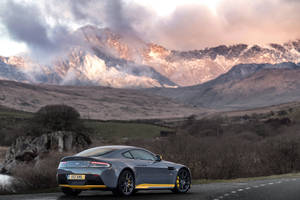 灰色 Aston Martin 跑車，帶有黃色飾邊，停泊在日落時分的山路上。 — 奧斯頓馬丁 壁紙
