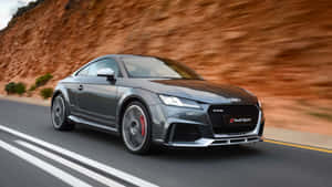 灰色 Audi TT RS 在岩石懸崖旁的道路上疾馳。 — 奧迪 GIF 壁紙