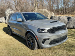 灰色 Dodge Durango SUV 停泊在戶外草地上，靠近大石頭和光禿禿的樹木。 — 道奇 壁紙