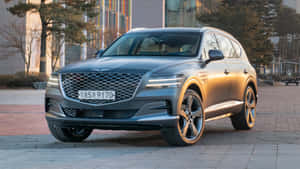 灰色 Genesis GV80 SUV 停放在鋪砌的廣場上，靠近現代建築和樹木。