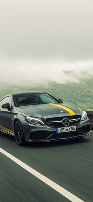 灰色 Mercedes-AMG 帶有黃色條紋在霧氣瀰漫的山路上行駛。 — iPhone 14 Plus 壁紙