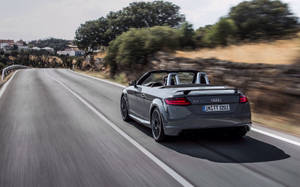 灰色Audi TT Roadster在彎曲的鄉村道路上快速行駛，背景有樹木和房屋。 — 奧迪 GIF 壁紙