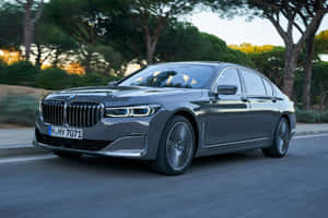 灰色BMW 7系列轎車在日落時分行駛在綠樹成蔭的道路上。 — MacBook Pro M2 壁紙