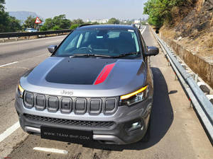 灰色Jeep Compass，帶紅色條紋，停在陽光明媚的高速公路旁，靠近綠樹和山丘。 — 吉普 壁紙