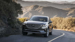 灰色Mazda CX-9 SUV在日出時行駛在蜿蜒的山路上。 — 馬自達 壁紙