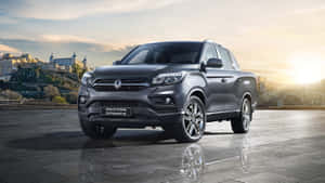 灰色SsangYong Rexton Sports皮卡車停在濕石廣場上，金色夕陽下以歷史城鎮為背景。 — 低調 壁紙
