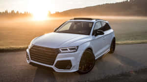 白色 Audi SQ5 SUV 在日出時停泊在霧氣瀰漫的道路上，背後是森林覆蓋的山丘。 — 奧迪 GIF 壁紙