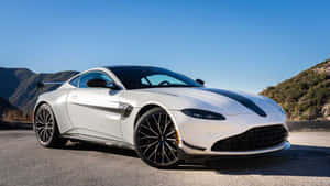 白色Aston Martin跑車帶黑色條紋，停在藍天下的山路。 — 奧斯頓馬丁 壁紙