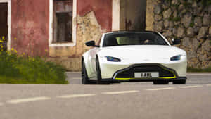 白色Aston Martin跑車停泊在紅色建築和石牆旁邊。 — 奧斯頓馬丁 壁紙