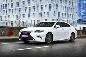 白色Lexus ES 200轎車在街道上行駛，背景是玻璃建築。 — 白色 iPhone 壁紙