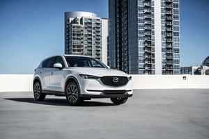 白色Mazda CX-5 SUV停放在城市屋頂上，背景是高聳的玻璃建築。 — 馬自達 壁紙