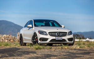 陽光明媚的日子裡，白色Mercedes-AMG C63停泊在靠近山脈的碎石路上。