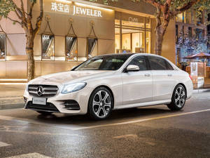 夜間白色賓士E-Class轎車停泊在濕潤的城市街道上，靠近珠寶店。 — 城市 壁紙