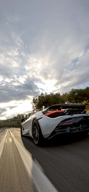 白色跑車在日落時分的道路上奔馳，天空有戲劇性的雲彩 — iPhone 11 Pro 壁紙