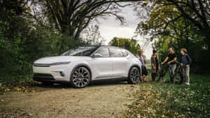 一家大小騎著腳踏車在秋林中欣賞白色電動SUV。 — 克萊斯勒 壁紙