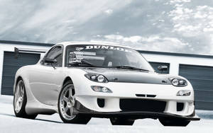 白色馬自達RX-7跑車，帶有黑色引擎蓋和賽車貼紙，停放在車庫前。 — 馬自達 壁紙