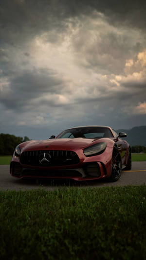 紅色 Mercedes-AMG GT 跑車停泊在路邊，天空風起雲湧。 — 深色 iPhone 壁紙