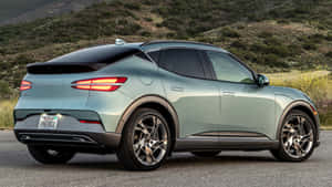 薄荷綠色 Genesis GV60 電動 SUV 停在山丘和野花附近的道路上。 — 創世紀 壁紙