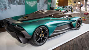 在室內活動中展示的藍綠色和黑色Aston Martin hypercar。 — 奧斯頓馬丁 壁紙