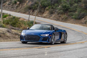 藍色Audi R8 Spyder在彎曲的山路上行駛，周圍是綠色的山坡。 — 奧迪 GIF 壁紙