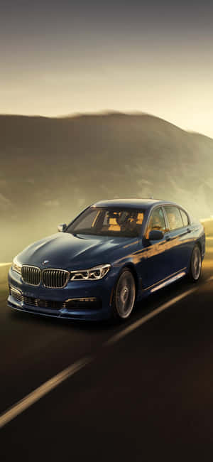 日落時分，藍色BMW轎車在山路上行駛。 — Redmi Note 14 Pro 壁紙