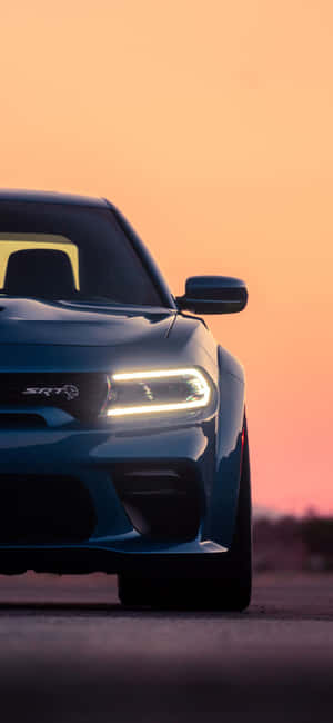 藍色Dodge SRT汽車在日落時分於道路上亮起車頭燈。 — Galaxy A18 壁紙