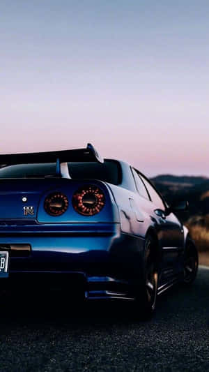 藍色跑車帶有發光尾燈，停泊在黃昏的山路上。 — 日產 Skyline GTR R34 壁紙