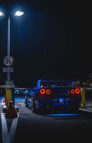 夜間收費站的藍色跑車，帶有發光的紅色尾燈。 — 日產 Skyline GTR R34 壁紙