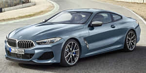 時尚的藍色BMW 8系列轎跑車行駛在蜿蜒的道路上，兩旁有礫石和綠樹。 — 奧迪R8 壁紙
