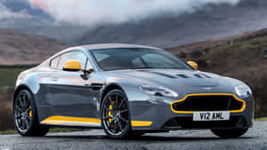 銀色 Aston Martin V12 AMR 帶黃色飾條，停泊在靠近山區的碎石路上。 — 奧斯頓馬丁 壁紙