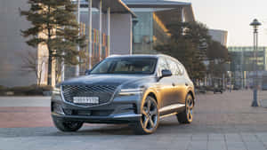 日落時分，銀色 Genesis GV80 SUV 停泊在現代建築前。 — 創世紀 壁紙