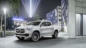 銀色 Mercedes-Benz 皮卡車在夜間停放在現代城市廣場，配有聚光燈和玻璃建築。 — 老福特卡車 壁紙