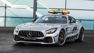銀色 Mercedes-AMG GT 安全車，帶有閃爍的燈光，停在室內玻璃牆附近。 — 賽車 壁紙