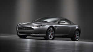 銀色Aston Martin跑車在工作室中，帶有戲劇性燈光和反光地板。 — 奧斯頓馬丁 壁紙