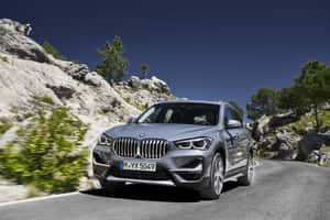 銀色BMW X1 SUV在岩石峭壁和樹木的山路上行駛。 — Surface Pro 壁紙