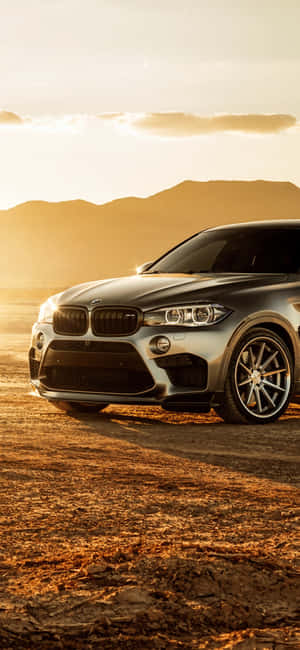 銀色BMW X6 SUV停放在金色夕陽下的沙漠中。 — Galaxy S25 Edge 壁紙