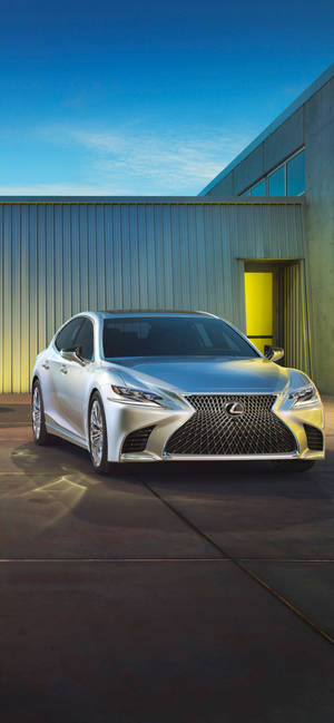 銀色Lexus轎車停在一座帶有黃色門的現代建築旁，藍天之下。 — iPhone 15 Plus 壁紙