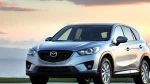 銀色Mazda CX-5 SUV停泊在日落時分的海邊，金色天空倒映。 — 馬自達 壁紙