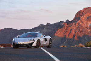 銀色McLaren GT6 MCL跑車在沙漠公路上，日落時分紅色山脈。 — 麥拉倫 壁紙