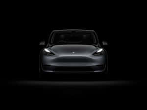 在黑暗工作室中，車頭燈照亮銀色Tesla Model 3的正面視圖。 — 特斯拉 壁紙