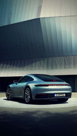 銀色保時捷911停在現代金屬面板建築前。 — 汽車 iPhone 壁紙