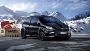 黑色 Abarth 500 Nitro 跑車停放在積雪的山路上，旁邊有滑雪裝備。 — 1600x900 壁紙