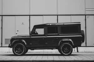 黑色 Land Rover Defender 停在工業建築旁的人行道上。 — MacBook Air 壁紙