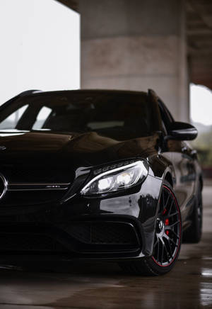 黑色 Mercedes-AMG 跑車帶有紅色點綴，停放在混凝土車庫中。 — Mercedes Amg iPhone 壁紙